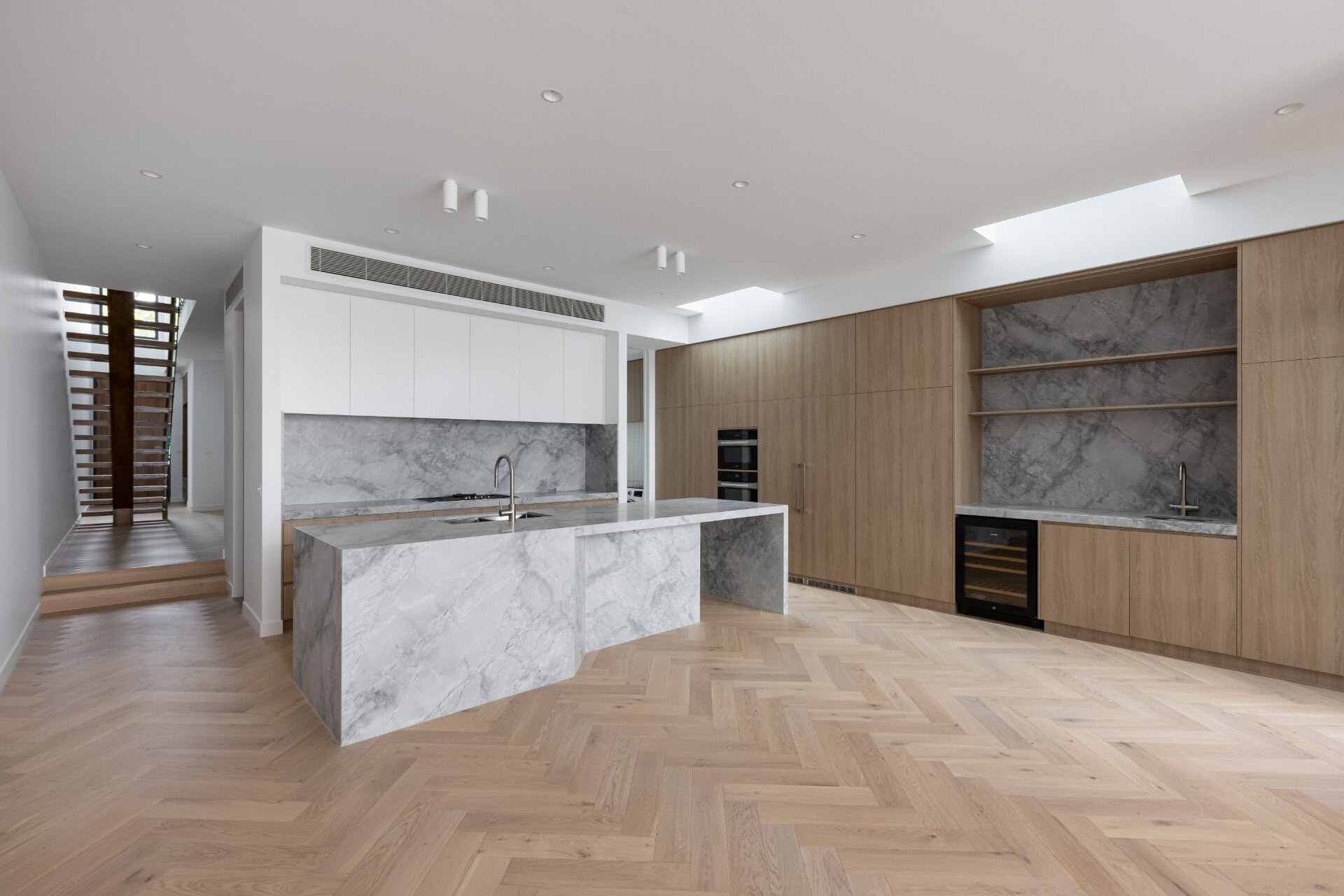 Open-plan kitchen with marble island, timber cabinetry, and built-in shelving with stone backing