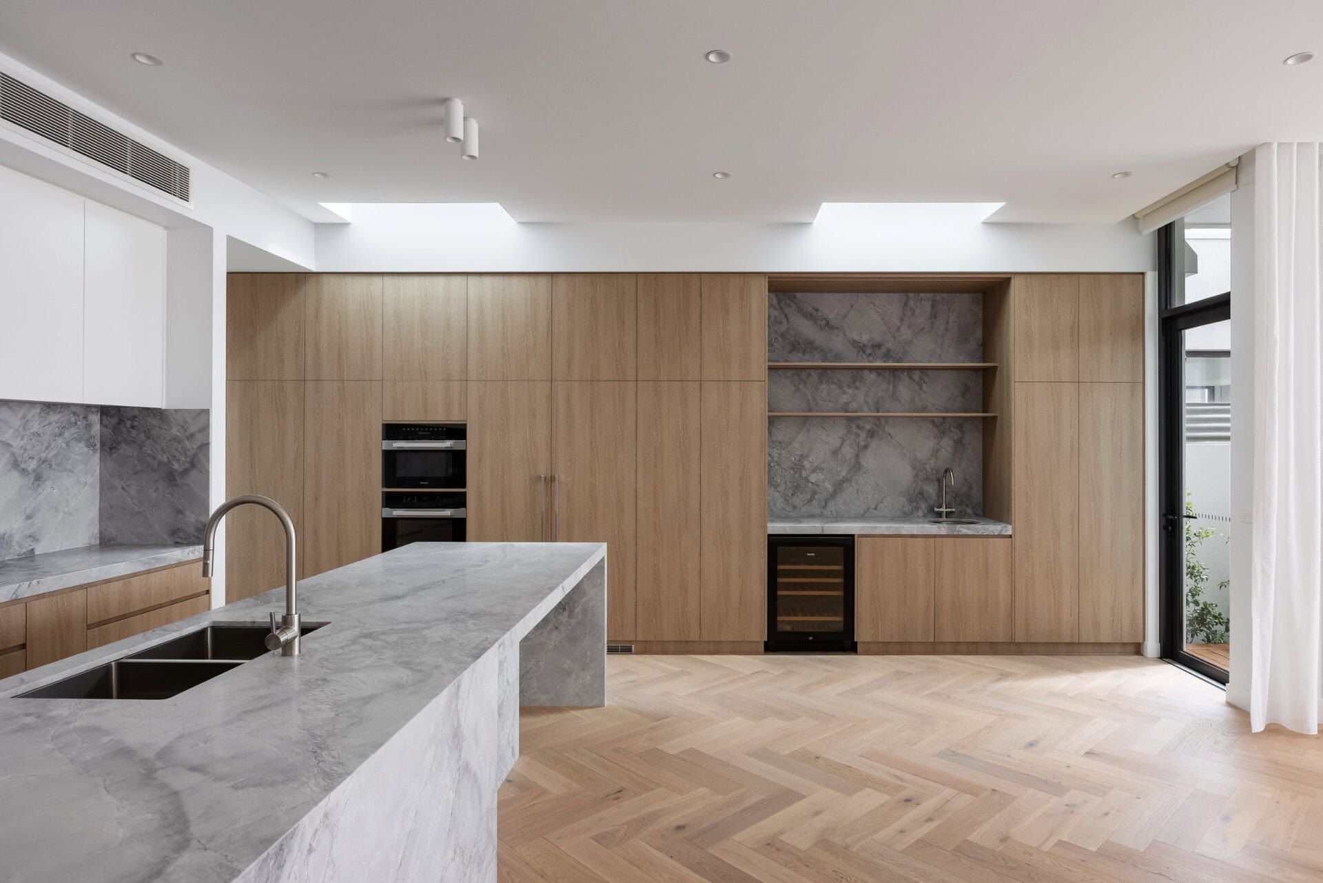 Modern kitchen with marble island, timber cabinetry, and built-in shelving with marble backing