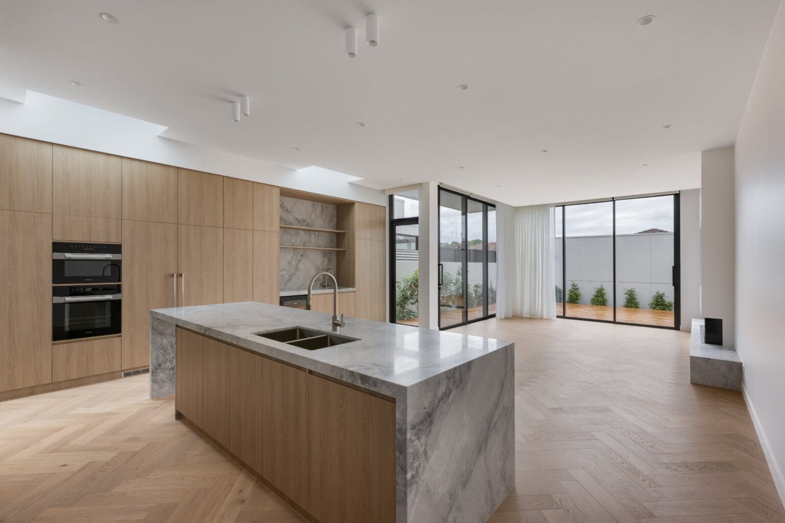 Open-plan kitchen and living area with marble island and large sliding doors to outdoor courtyard